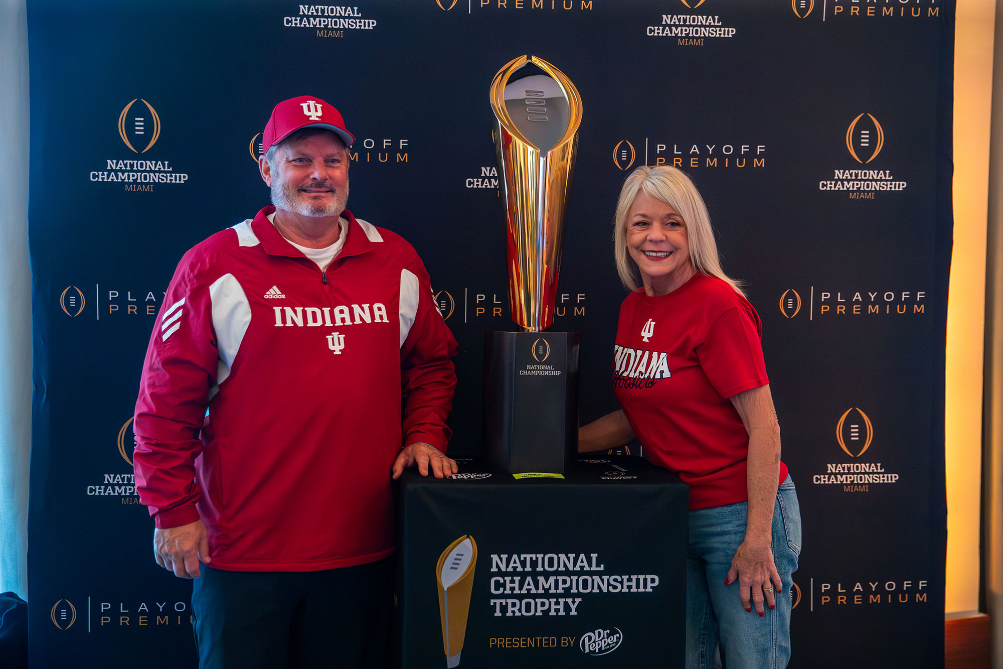 Two fans posing with the College Football Playoff National Championship trophy